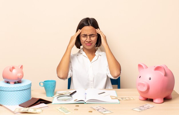 Jonge Latijns-vrouw kijkt geconcentreerd, bedachtzaam en geïnspireerd, brainstormend en verbeeldend met de handen op het voorhoofd