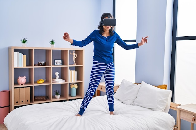 Jonge latijns-vrouw met behulp van virtual reality-bril staande op bed in de slaapkamer