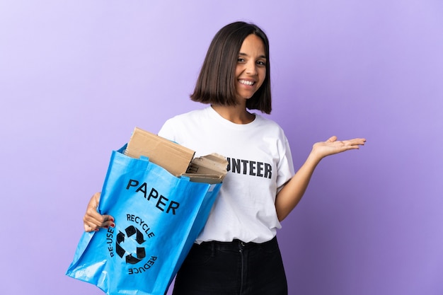 Jonge Latijns-vrouw met een recyclingzak vol papier om te recyclen geïsoleerd op paars met een idee terwijl ze glimlachend naar kijkt