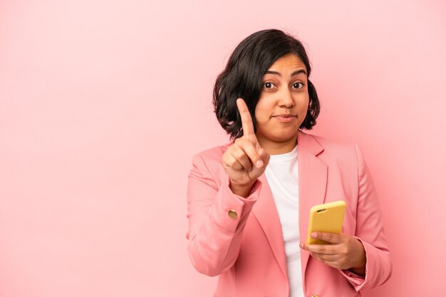 Jonge Latijns-vrouw met mobiele telefoon geïsoleerd op roze achtergrond met nummer één met vinger.