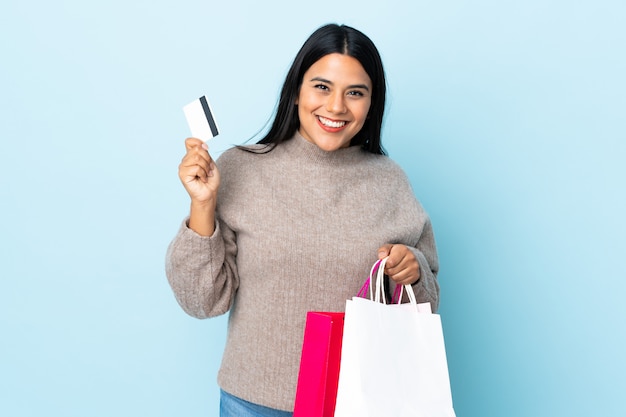 Jonge latijns-vrouw vrouw geïsoleerd op blauwe muur met boodschappentassen en een creditcard