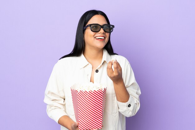 Jonge Latijns-vrouw vrouw geïsoleerd op een witte muur met 3D-bril en met een grote emmer popcorns