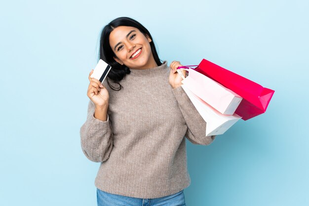 Jonge Latijns-vrouw vrouw op blauwe muur met boodschappentassen en een creditcard