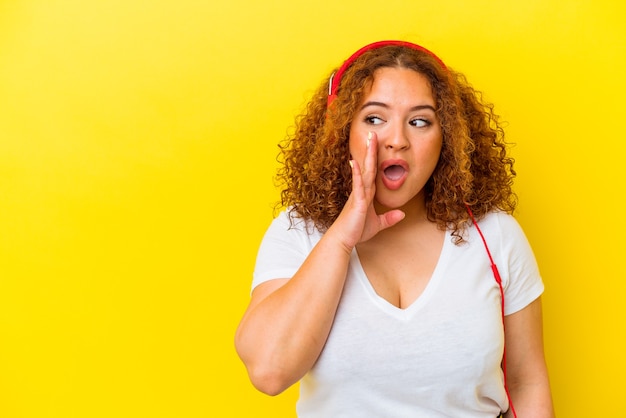 Jonge Latijnse bochtige vrouw die muziek luistert die op gele achtergrond wordt geïsoleerd, zegt een geheim heet remmend nieuws en kijkt opzij