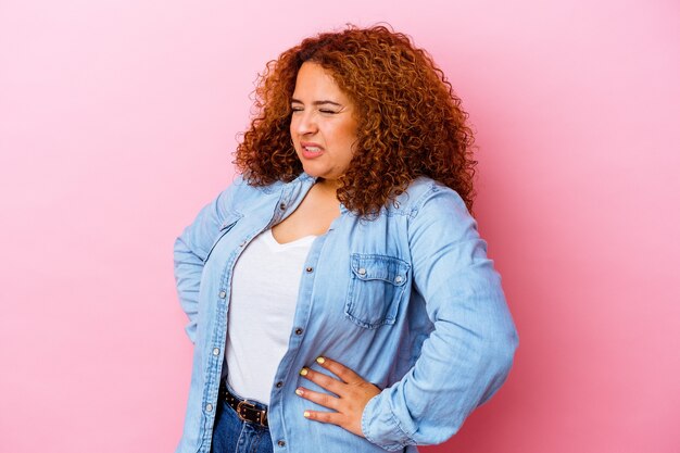 Jonge Latijnse bochtige vrouw die op roze muur wordt geïsoleerd die aan rugpijn lijdt.