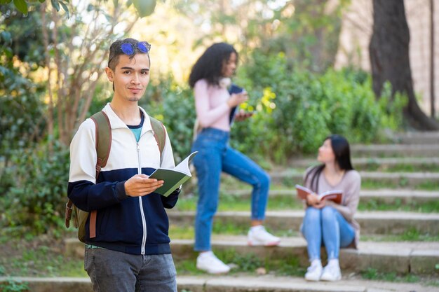 Jonge latijnse mannelijke student lacht en kijkt naar de camera met een notitieboekje in het park