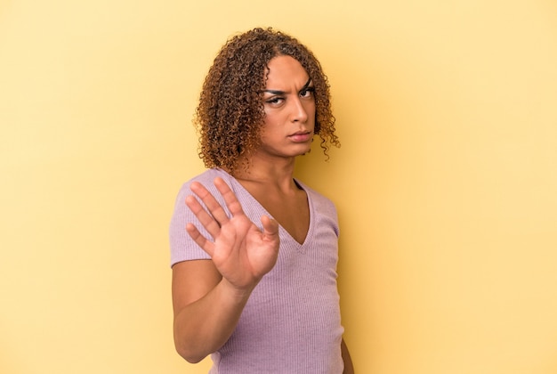 Jonge latijnse transseksuele vrouw geïsoleerd op een gele achtergrond die iemand afwijst die een gebaar van walging toont.