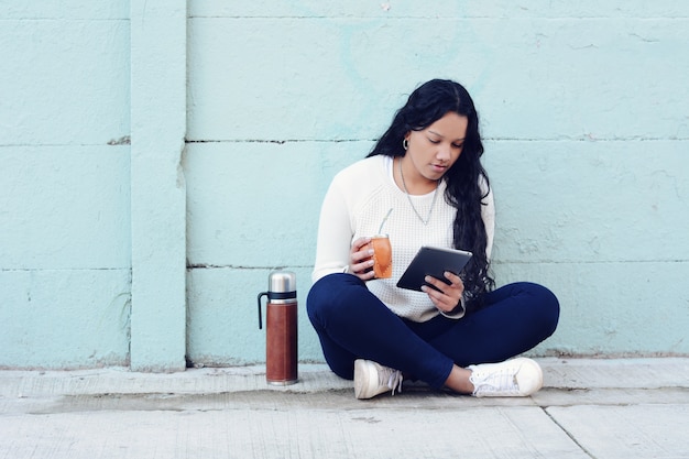 Jonge Latijnse vrouw die de traditionele thee van de Yerba Mate met tablet drinken