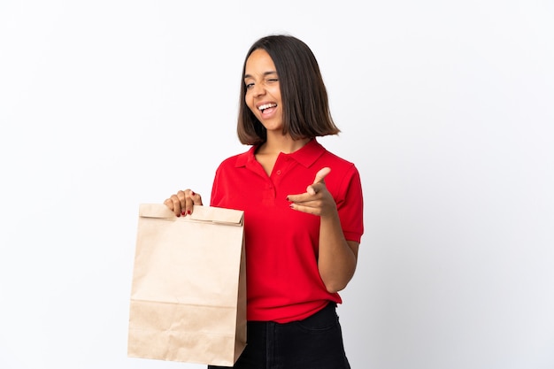 Jonge Latijnse vrouw die een boodschappentas houdt die op wit wordt geïsoleerd dat naar voren richt en glimlacht