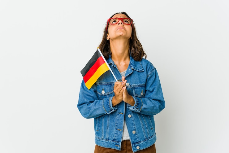 Foto jonge latijnse vrouw die een duitse vlag houdt die op witte muur wordt geïsoleerd die hand in hand bid dichtbij mond, voelt zich zelfverzekerd.