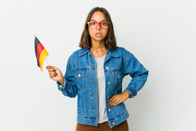 Jonge Latijnse vrouw die een Duitse vlag houdt die op witte ruimte wordt geïsoleerd die wordt geschokt wegens iets dat zij heeft gezien.