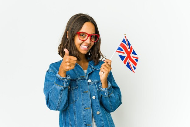 Jonge Latijnse vrouw die een Engelse vlag houdt die op wit wordt geïsoleerd dat en duim glimlacht opheft