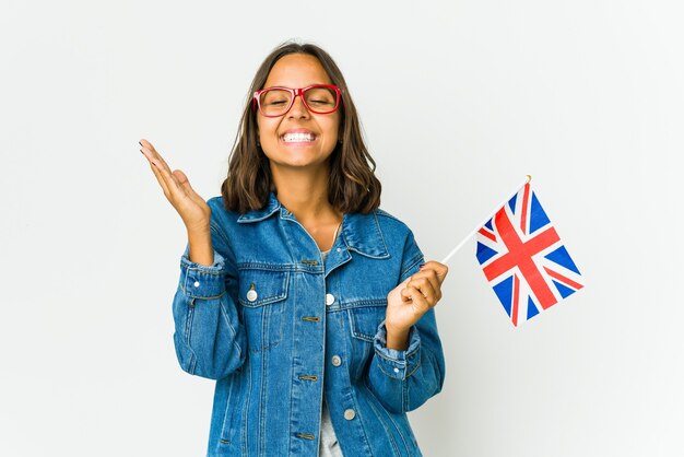 Jonge Latijnse vrouw die een Engelse vlag houdt die op witte muur wordt geïsoleerd vrolijk veel lachen. Geluk concept.