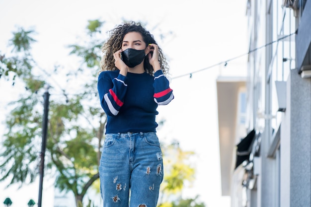 Jonge latijnse vrouw die een gezichtsmasker gebruikt terwijl ze buiten op straat aan de telefoon praat. Nieuwe normale levensstijl. Stedelijk begrip.