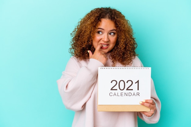 Jonge latijnse vrouw die een kalender houdt die op blauwe muur wordt geïsoleerd, ontspant het denken over iets dat een exemplaarruimte bekijkt