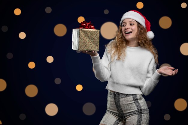 Jonge latijnse vrouw die een kerstcadeau toont met een kerstmanhoed. ruimte voor tekst.