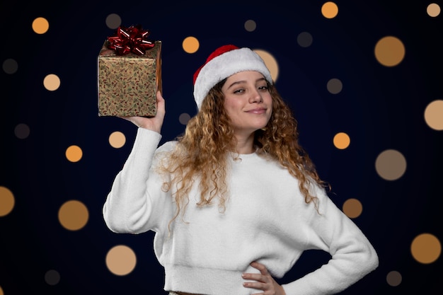 Jonge latijnse vrouw die een kerstcadeau toont met een kerstmanhoed. ruimte voor tekst.