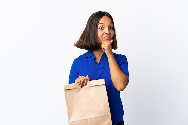 Jonge Latijnse vrouw die een kruidenierswinkel het winkelen zak houdt die bij wit wordt geïsoleerd denken