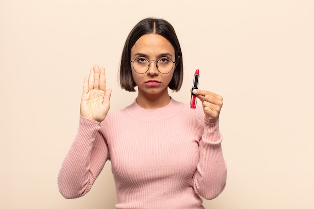 Jonge Latijnse vrouw die ernstig, streng, ontevreden en boos kijkt die open palm toont die stopgebaar maakt