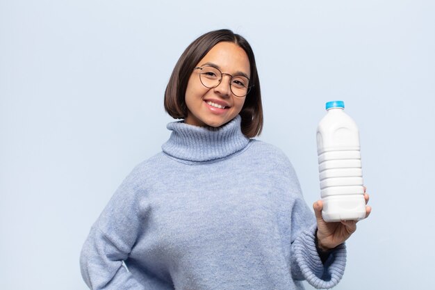 Jonge Latijnse vrouw die gelukkig glimlacht met een hand op heup en zelfverzekerde, positieve, trotse en vriendelijke houding