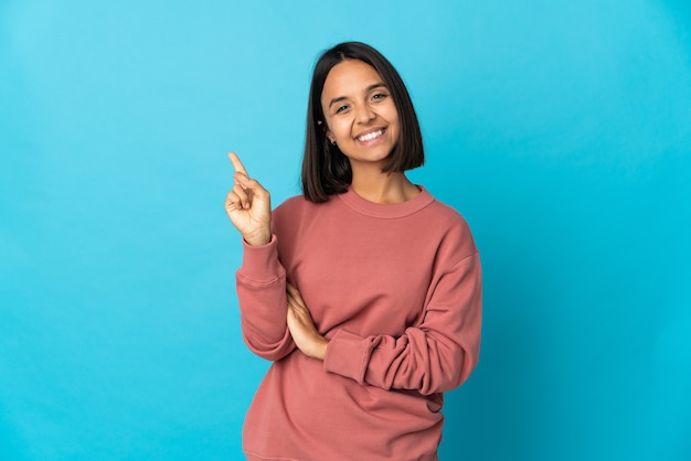 Jonge Latijnse vrouw die op blauwe muur wordt geïsoleerd die en een vinger in teken van het beste opheft