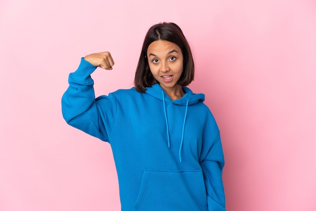 Jonge Latijnse vrouw die op roze muur wordt geïsoleerd die sterk gebaar doet