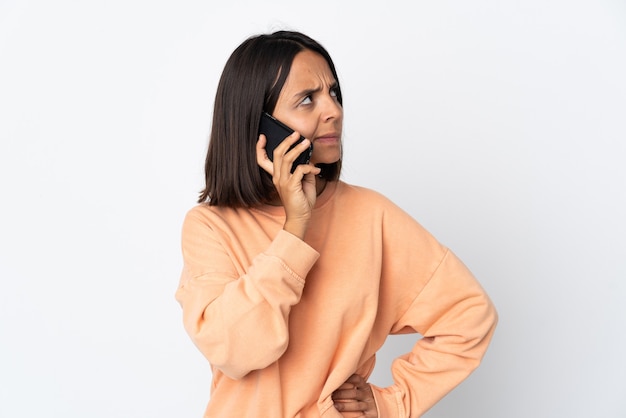 Jonge Latijnse vrouw die op witte muur wordt geïsoleerd die een gesprek met de mobiele telefoon met iemand houdt