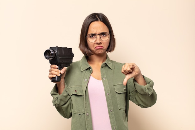 Jonge Latijnse vrouw die zich boos, boos, geïrriteerd, teleurgesteld of ontevreden voelt, duimen naar beneden toont met een serieuze blik