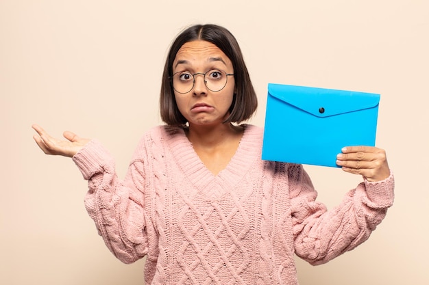 Jonge latijnse vrouw die zich verward en verward voelt, twijfelt, weegt of verschillende opties kiest met grappige uitdrukking