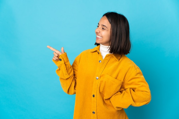 Jonge latijnse vrouw geïsoleerd op een blauwe achtergrond die met de vinger naar de zijkant wijst en een product presenteert