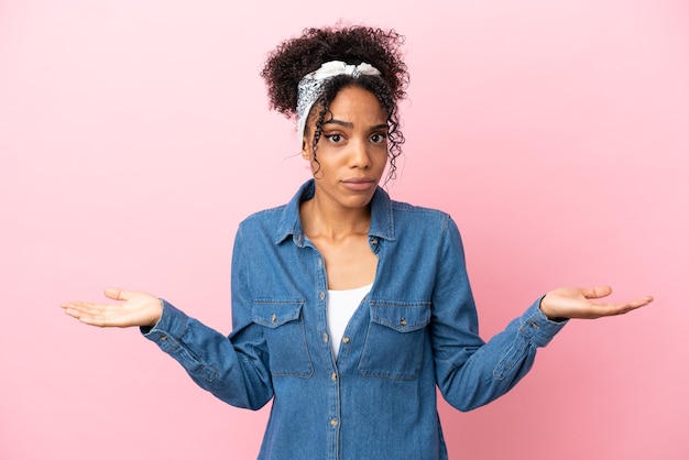 Jonge latijnse vrouw geïsoleerd op roze achtergrond die twijfels heeft terwijl ze haar handen opsteekt