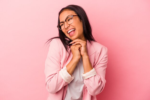 Jonge latijnse vrouw geïsoleerd op roze achtergrond houdt handen onder de kin, kijkt gelukkig opzij.