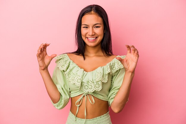 Foto jonge latijnse vrouw geïsoleerd op roze achtergrond met iets met palmen, aanbieden aan camera.