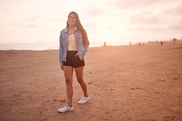 Jonge latijnse vrouw glimlacht tijdens een prachtige zonsondergang gelukkige jonge vrouw met masker op het strand