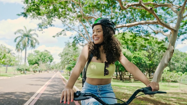 Jonge Latijnse vrouw in beschermende helm rijdt op haar fiets langs het fietspad in een stadspark