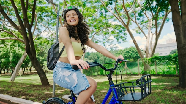 Jonge Latijnse vrouw in beschermende helm rijdt op haar fiets langs het fietspad in een stadspark