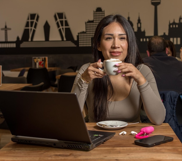 jonge Latijnse vrouw in bruine top werkt of studeert op laptop pc computer drink koffie zitten aan tafel