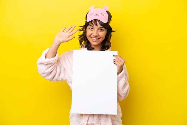 Jonge latijnse vrouw in pyjama geïsoleerd op gele achtergrond met een leeg bordje en saluting