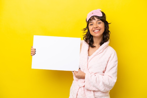 Jonge latijnse vrouw in pyjama geïsoleerd op gele achtergrond met een leeg bordje met gelukkige uitdrukking