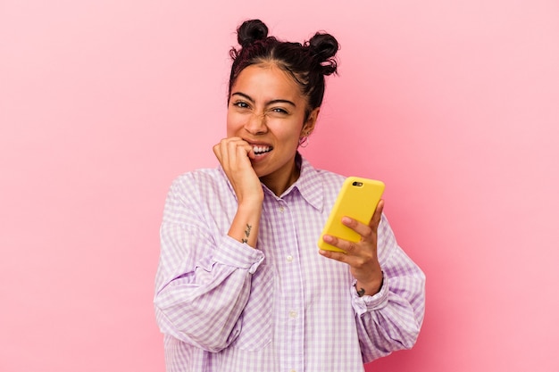 Jonge latijnse vrouw met een mobiele telefoon geïsoleerd op roze achtergrond bijtende vingernagels, nerveus en erg angstig.