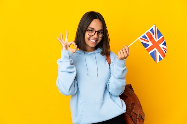 Jonge latijnse vrouw met een vlag van het Verenigd Koninkrijk geïsoleerd op een geel oppervlak met ok teken met vingers