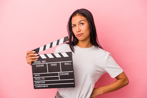 Jonge latijnse vrouw met Filmklapper geïsoleerd op roze achtergrond verward, voelt zich twijfelachtig en onzeker.