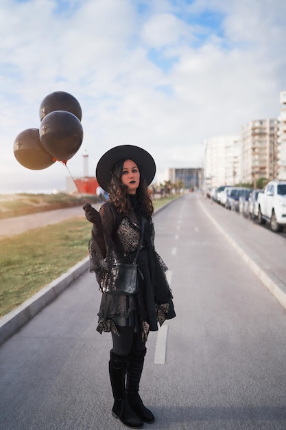 Jonge latijnse vrouw verkleed als een heks die op straat staat met ballonnen portrait