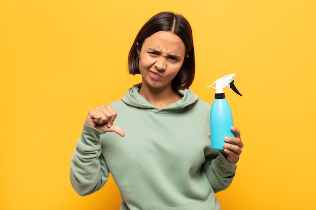Jonge latijnse vrouw voelt zich boos, boos, geïrriteerd, teleurgesteld of ontevreden, duimen naar beneden met een serieuze blik