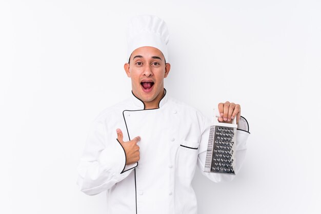 Jonge latin chef-kok man geïsoleerd verrast wijzend op zichzelf, breed glimlachend.