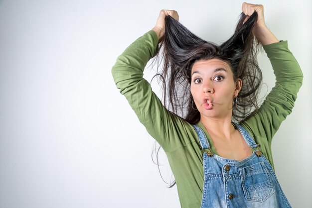 Jonge latina maakt een grappig gezicht en grijpt haar kapper thuis heel lang haar op neutrale achtergrond