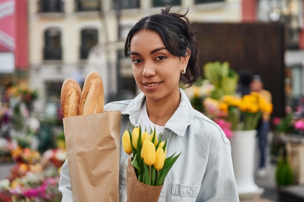 Jonge Latina-vrouw die lacht terwijl ze gele tulpen en brood koopt bij een straatverkoper