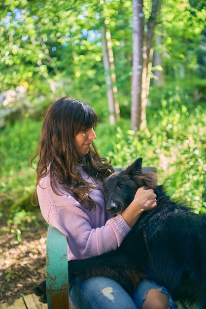 Jonge latina-vrouw knuffelt haar hond terwijl ze op een vintage turquoise stoel buiten haar huis zit