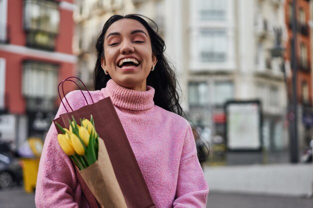 Jonge Latina-vrouw met gele tulpen en wijn die liefde en vreugde verspreidt door een romantische verrassing