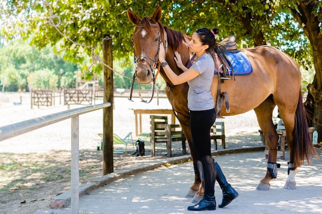 Jonge latina-vrouwenruiter die haar paard in het veld streelt